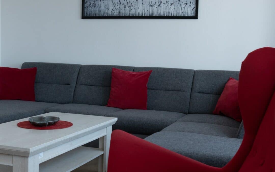 Czerwony fotel i narożna sofa w salonie apartamentu